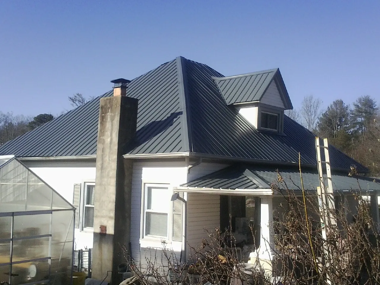 Dark blue standing seam metal roof on a white farmhouse with dormer — Slate & Tile Roof Repair by Roofing Brothers in Lorain