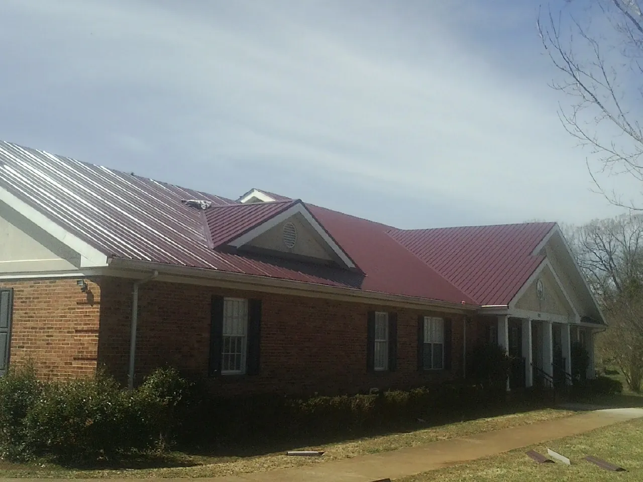 Red metal roof with gabled entries on a long brick building, from a Hail Damage Roof Repair job in Lorain