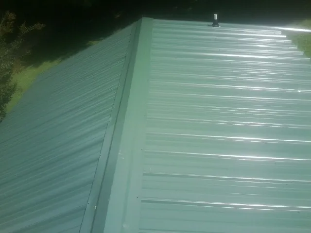 New green metal panels meeting at the ridge of a roof — Flat Roof Repair work by our crew in Lorain