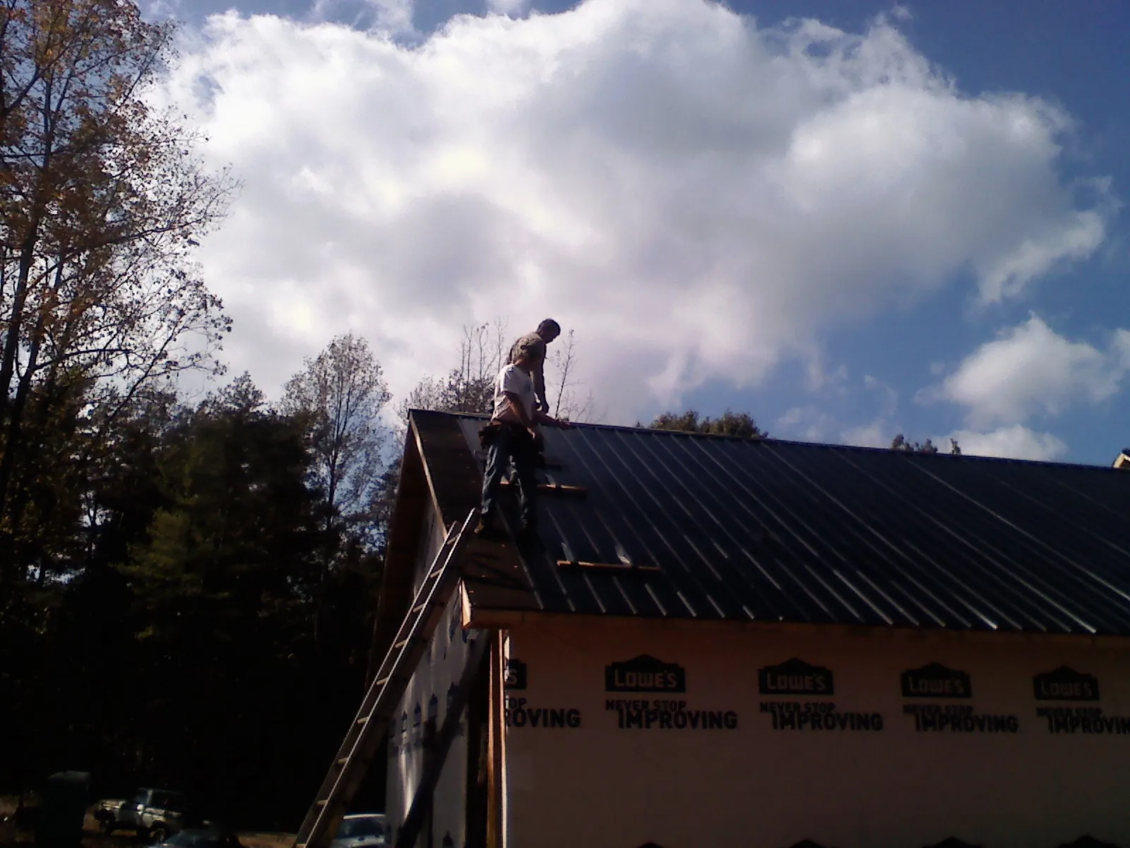Roofer fastening dark metal panels high against a cloudy sky, from a Roof Inspection job in Lorain