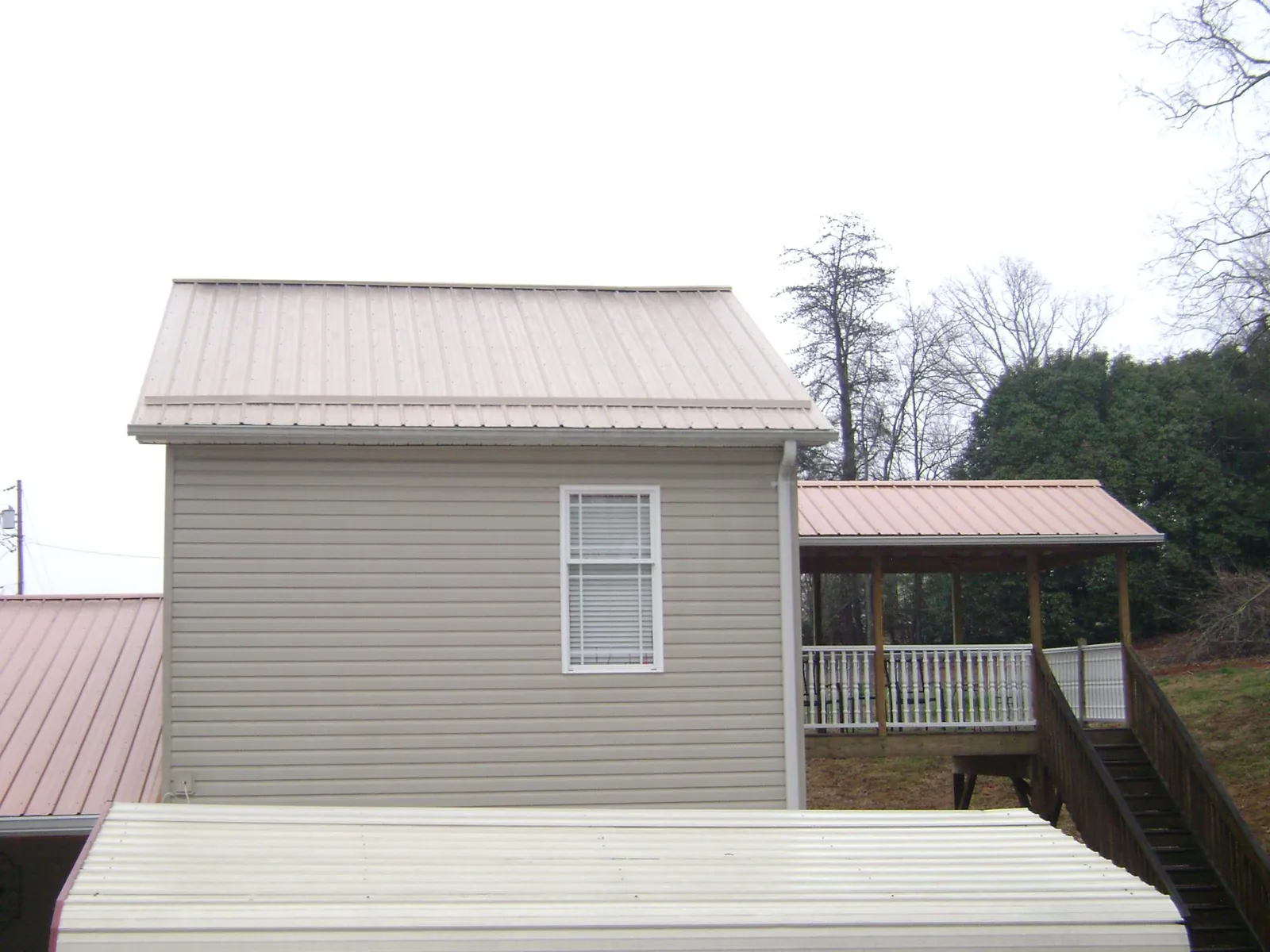 Tan metal roofs on a two story addition and attached porch, from a Roof Replacement job in Lorain